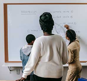 Lehrerin unterrichtet zwei Kinder an einer Tafel in Nigeria, gefördert durch Kinderschimmer e.V. für Bildung und Zukunftschancen