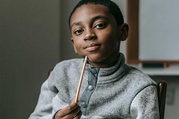 Nigerianischer Schüler denkt nach und hält einen Bleistift, Symbol für Bildung und Hoffnung durch Kinderschimmer e.V.